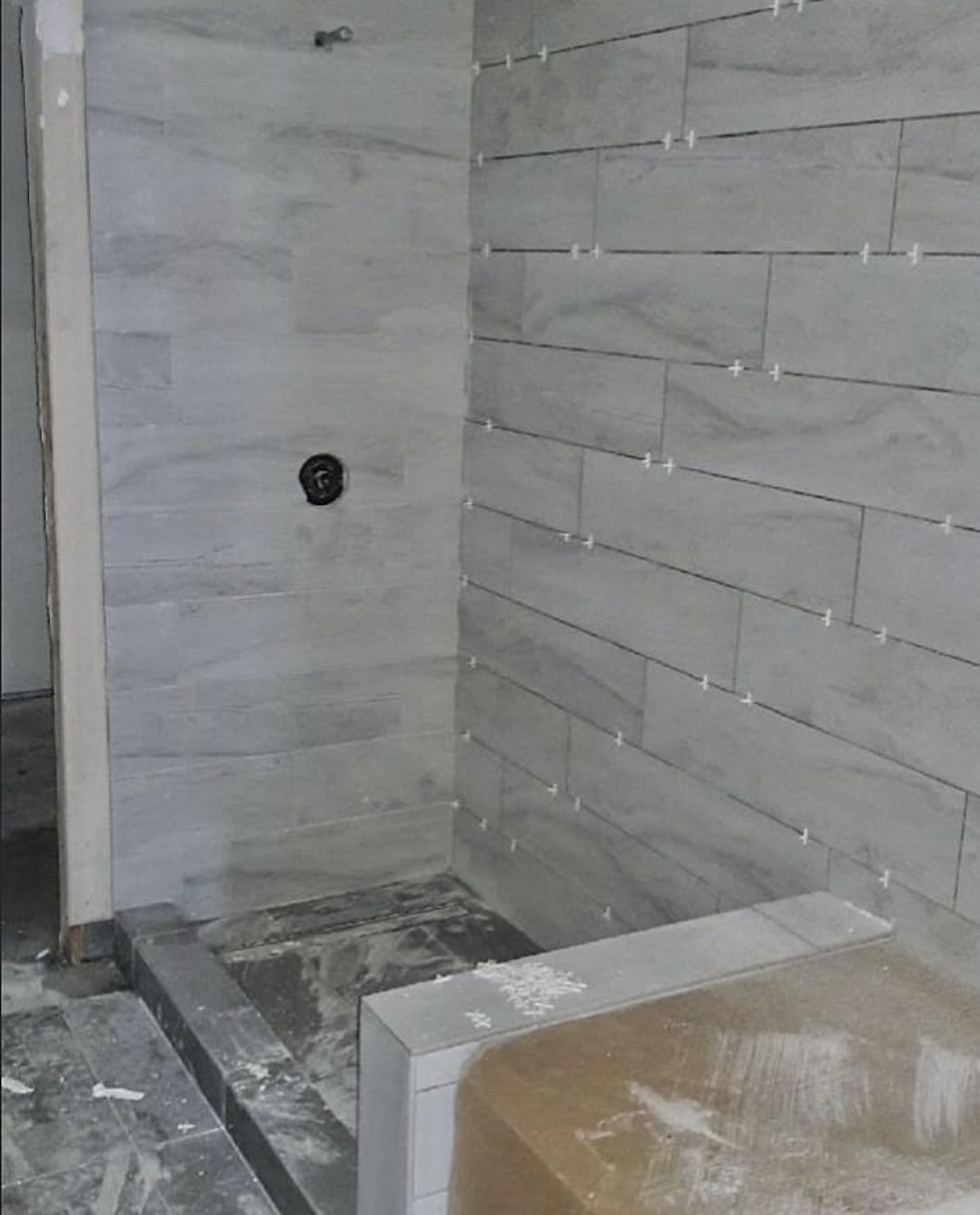 Tiled shower with curb and bench before glass